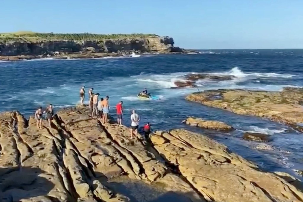 Las personas cerca del océano miran al nadador que fue devorado por un gran tiburón blanco, mientras las autoridades ordenaban a las personas que se mantuvieran alejadas del agua.