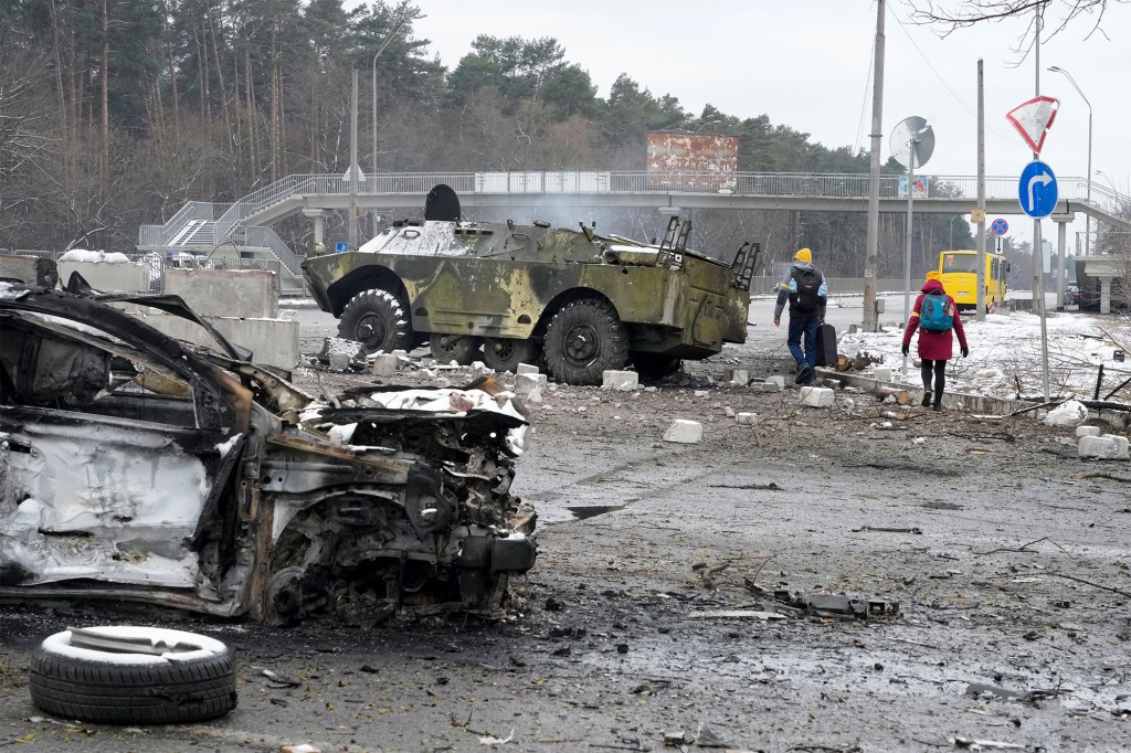 La gente camina con un vehículo destruido y un vehículo blindado en un puesto de control en Brovary, en las afueras de Kiev, Ucrania, el martes 1 de marzo de 2022.