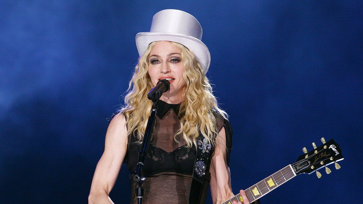Madonna lleva un sombrero blanco y toca la guitarra en concierto.