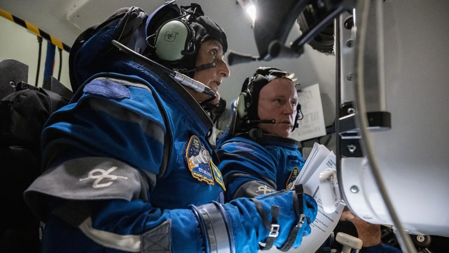 Dos astronautas con trajes espaciales miran pantallas en un simulador