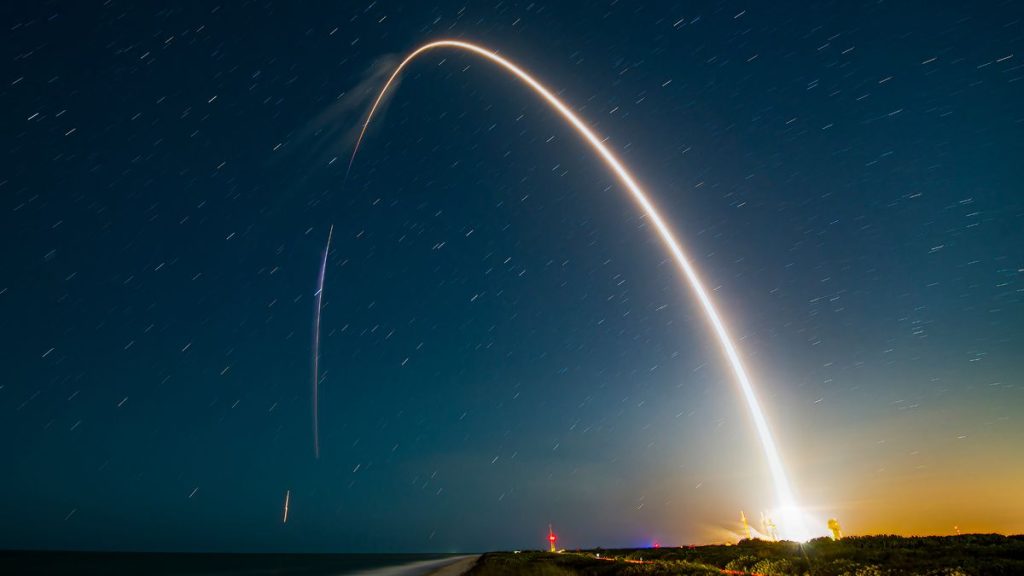 A rocket launch carves an orange arc into a dark night sky in this long-exposure photo.